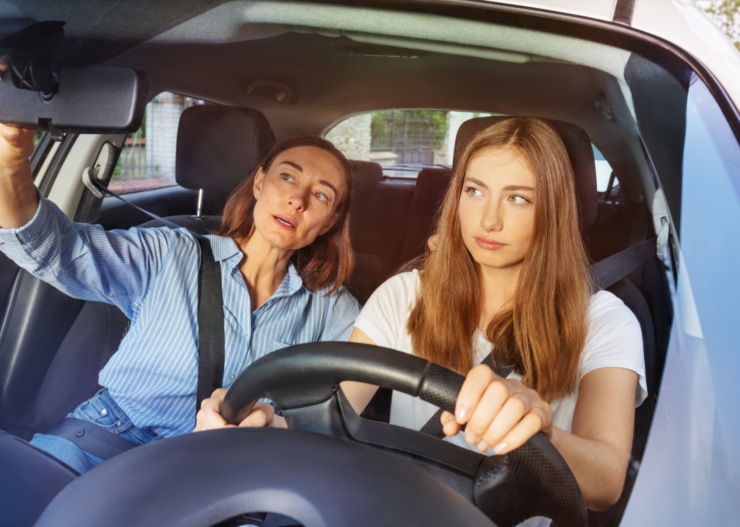 A parent teaching their child to adjust their mirrors while driving.